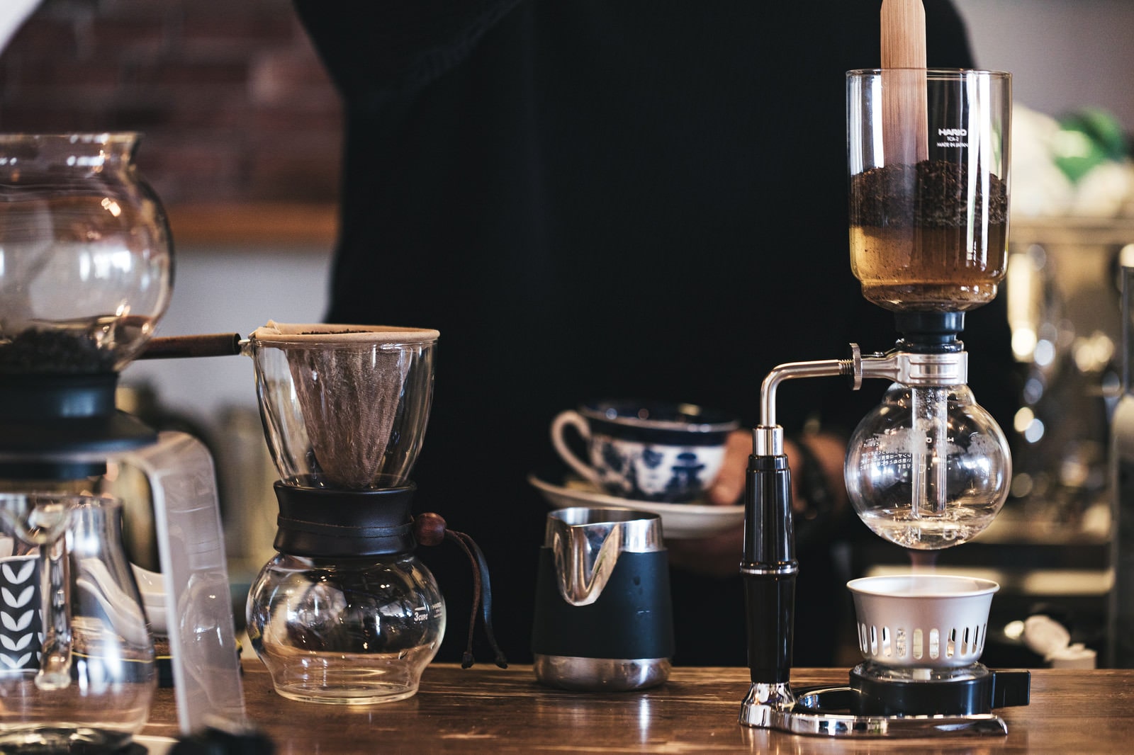 A siphon coffee maker with boiled water raised to the top chamber and coffee beans poured on a counter